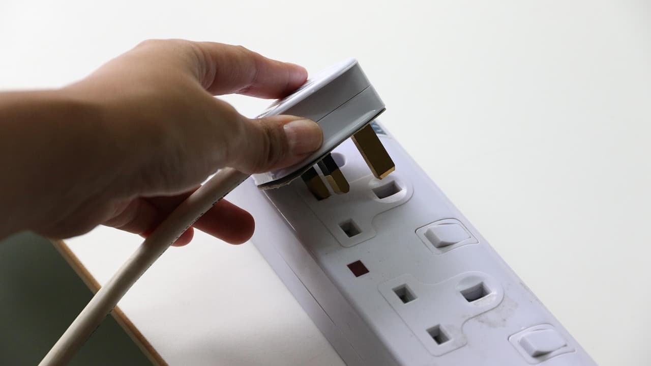 A UK three-pin plug going into a white socket strip