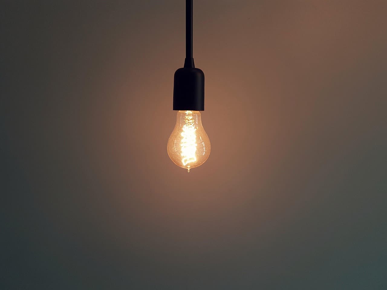 A single bulb glowing on a pendant against a plain wall
