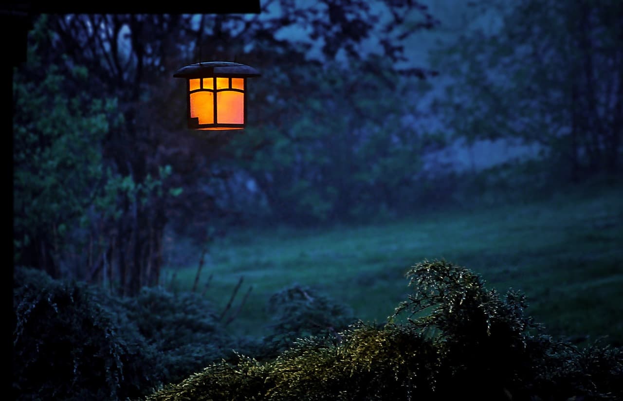 A lit outdoor lantern in a garden at dusk