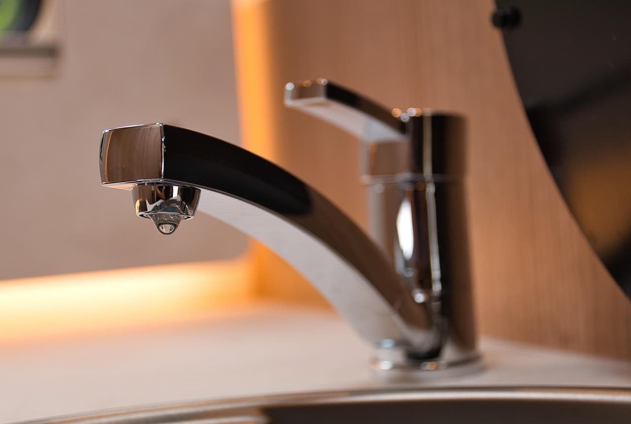 A chrome mixer tap over a sink in warm light